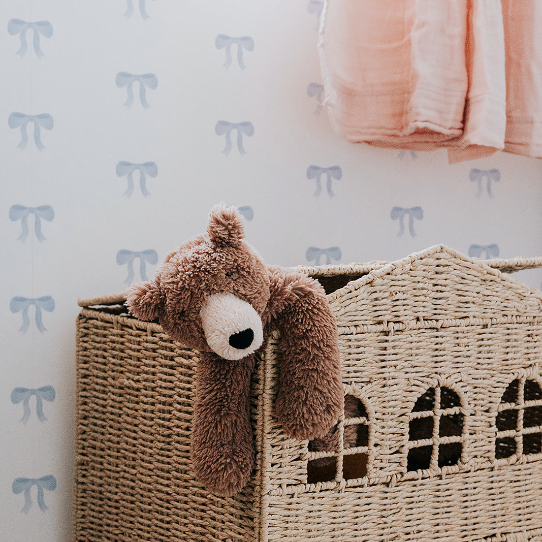 Hand-painted blue watercolour bow wallpaper decorates the wall of this children's room with dollhouse and teddy bear sitting in front