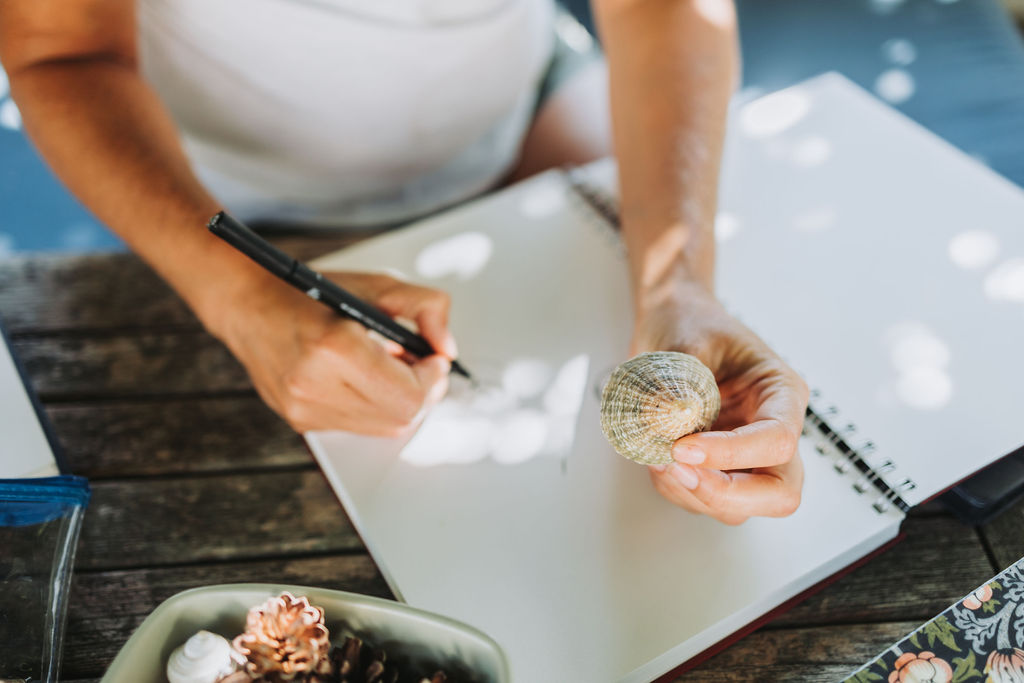 Katie holds a shell that she is drawing while sat in a summer green garden.